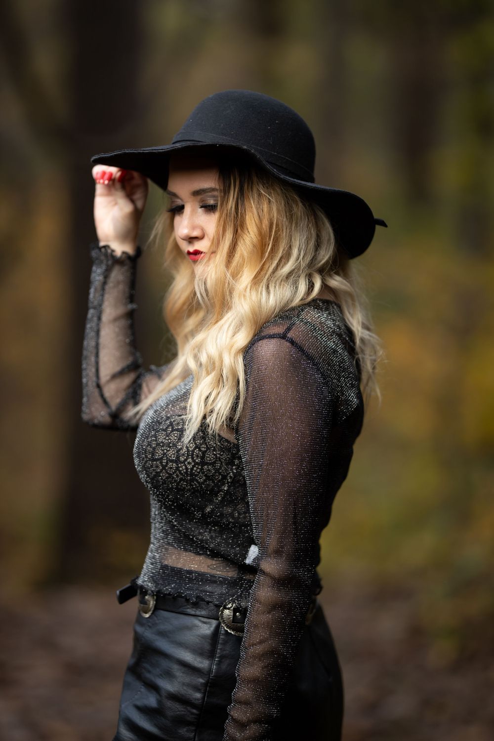Moody autumn fashion portrait featuring dark hat, sheer sleeves and leather details in a forest setting.
