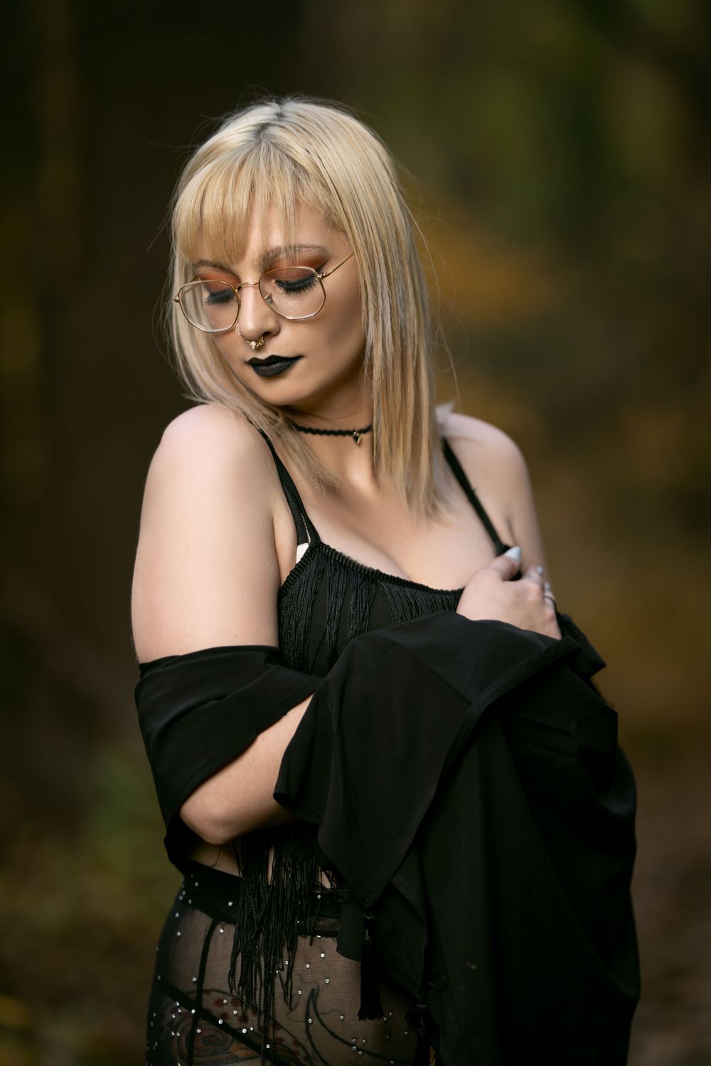 A moody fashion portrait featuring black clothing, choker necklace, and dark lipstick in a forest setting.