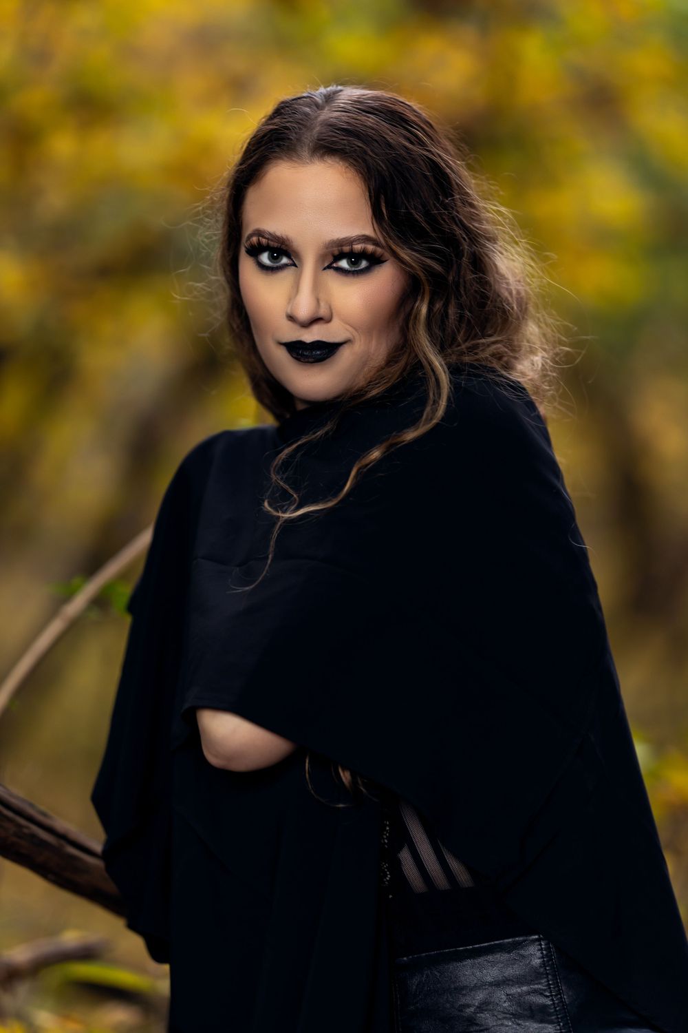 Dark gothic fashion portrait with dramatic makeup against autumn foliage background.