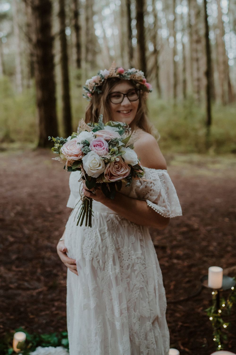 Soft pink roses complement a white lace wedding dress in a forest setting.