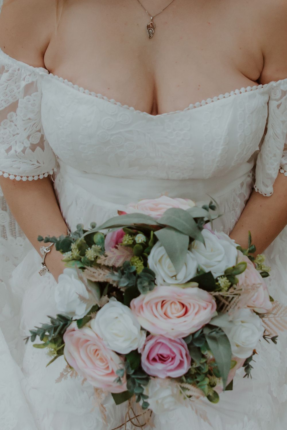 A delicate white lace wedding dress bodice with a bouquet of pink and white roses with greenery.