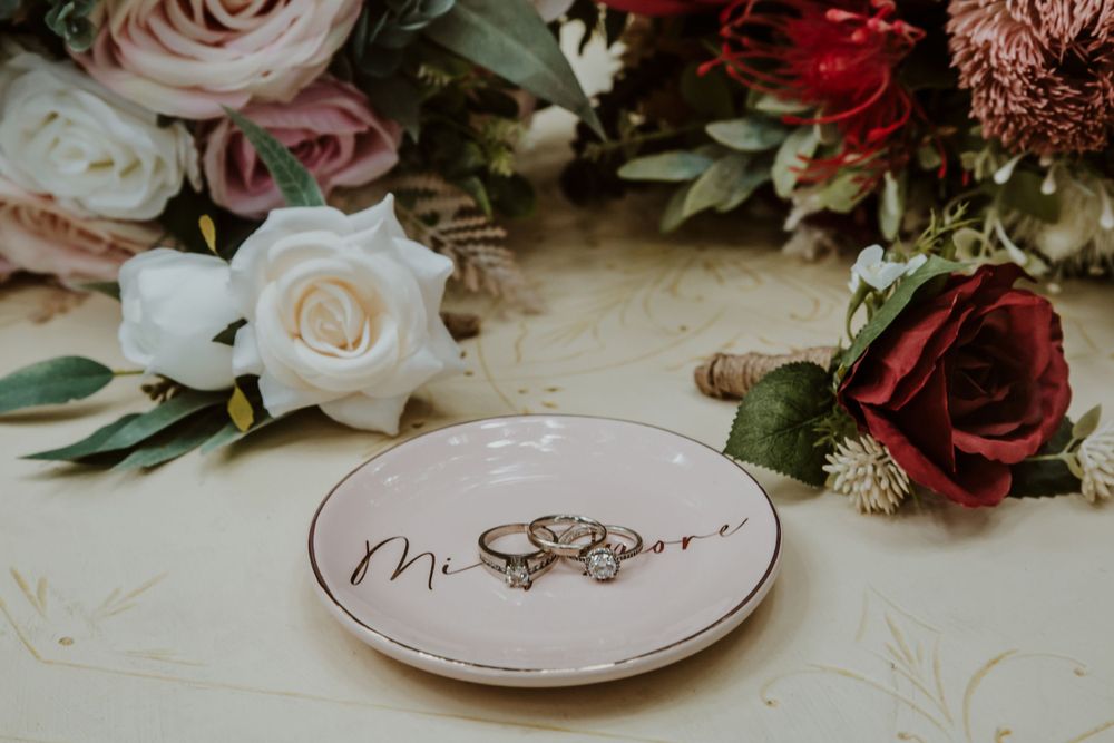Wedding rings displayed on a decorative plate surrounded by roses and floral arrangements.
