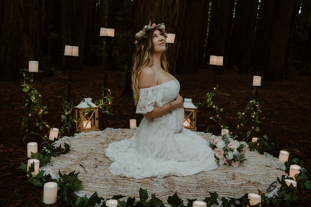 An ethereal forest wedding scene with candles and lanterns surrounding a white lace dress.