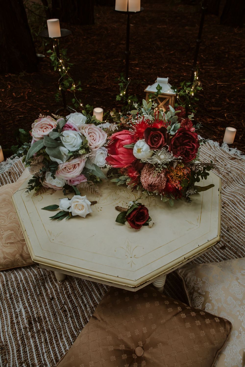 Wedding floral arrangements with red and pink roses on a white hexagonal table with pillows.