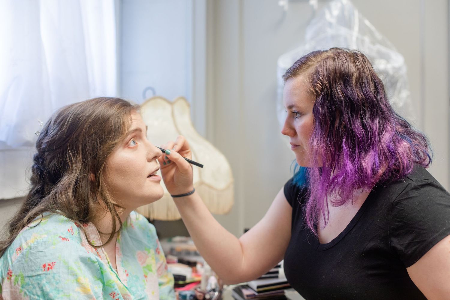 A makeup artist with colorful hair applies cosmetics during wedding day preparations.