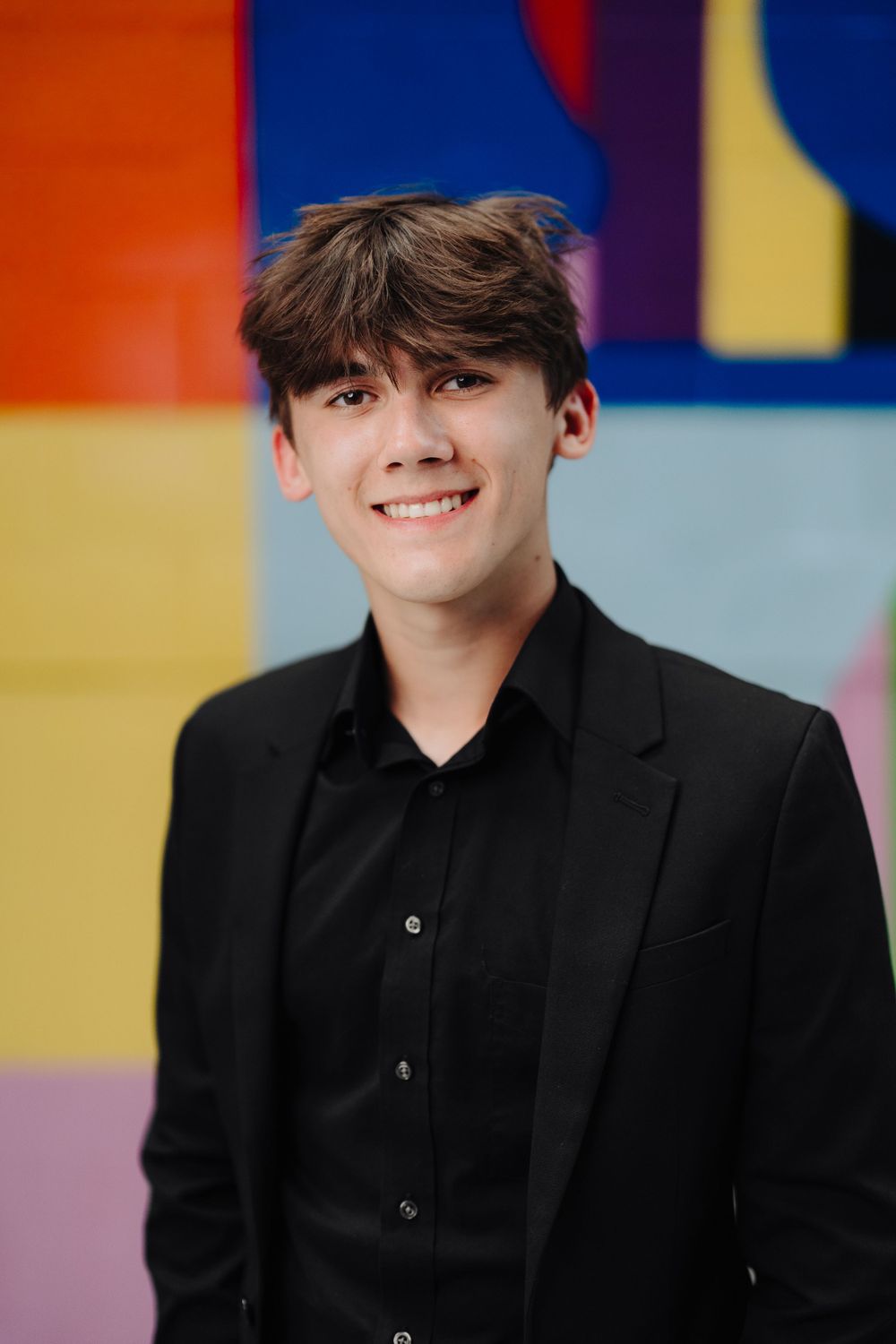 Portrait against colorful geometric wall background wearing all black formal attire.