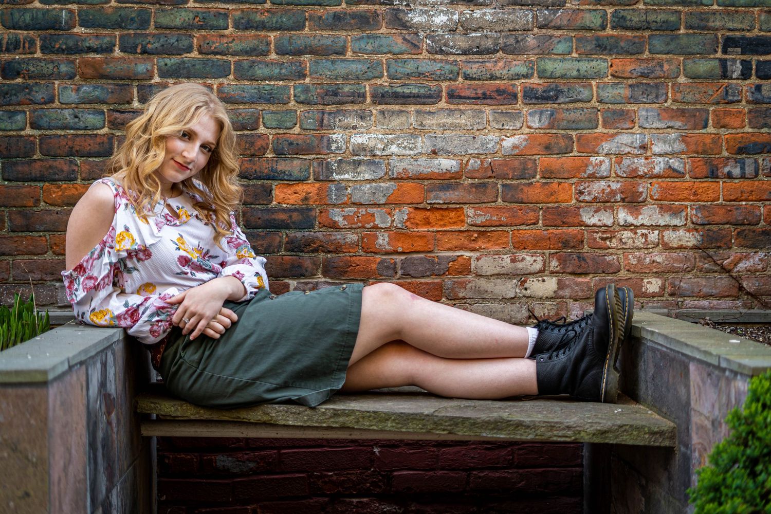 Young woman poses casually on bench with rough brick background