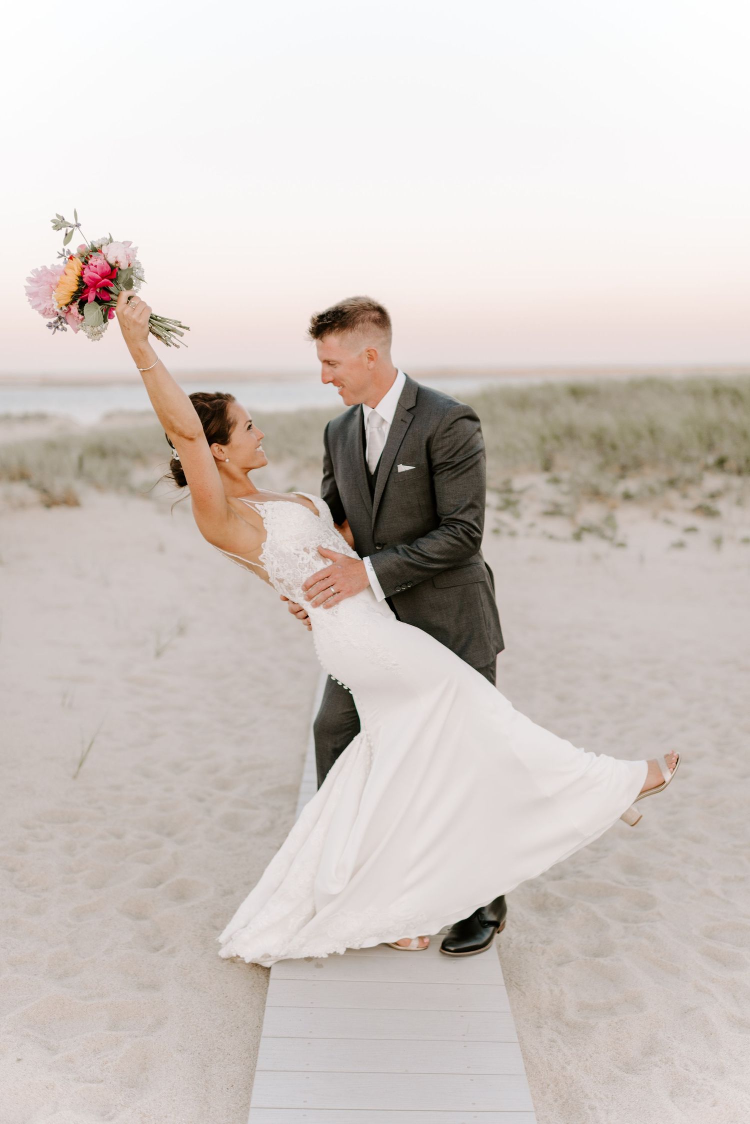 Couple dancing on beach boardwalk during wedding photoshoot with flowing white dress.