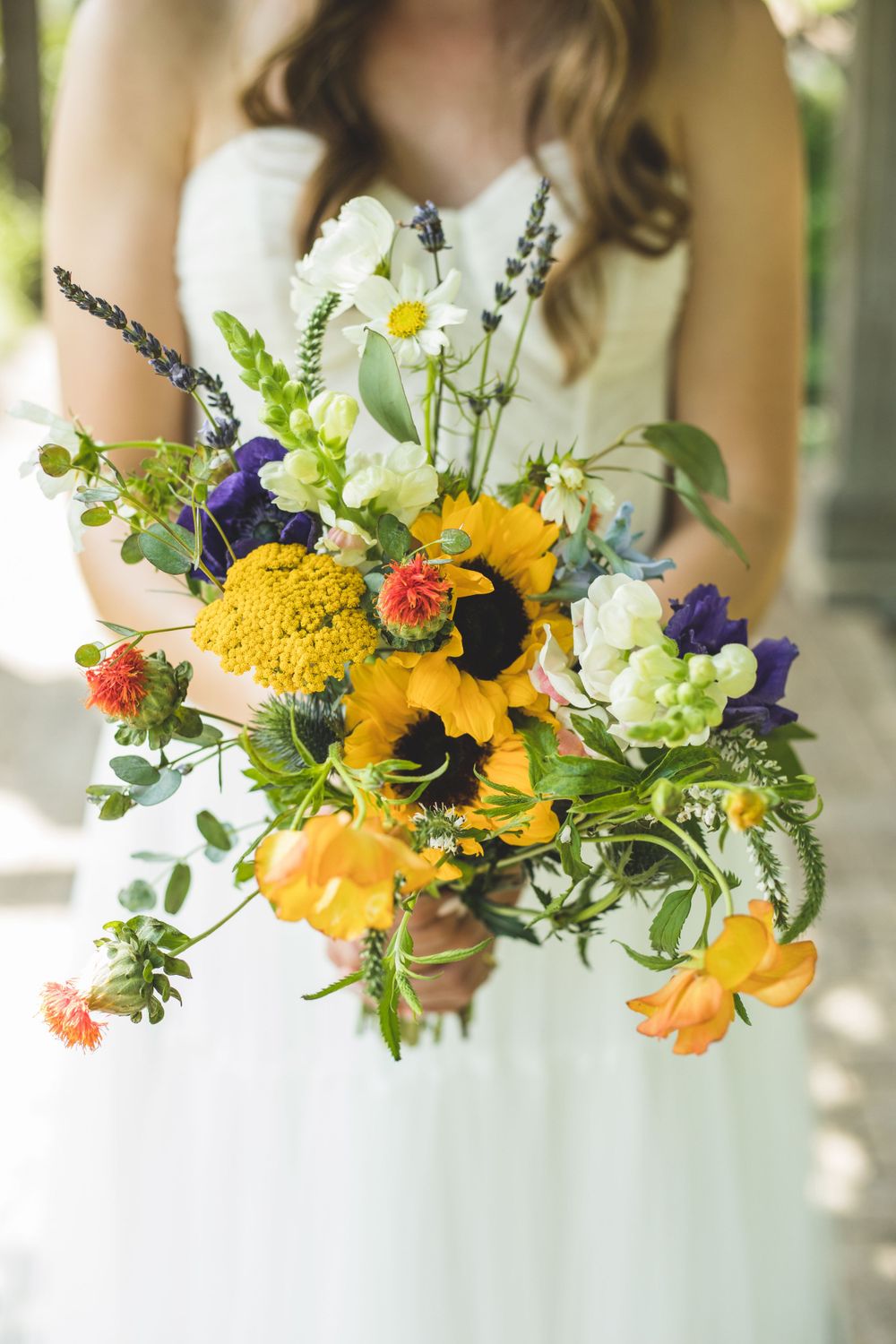 Vibrant wedding bouquet with sunflowers, wildflowers and colorful blooms against white dress.
