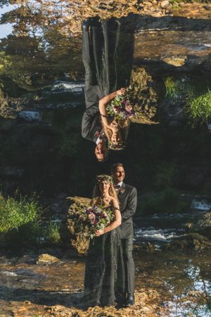 Creative mirror reflection portrait of two people in black dresses holding flower bouquets outdoors.