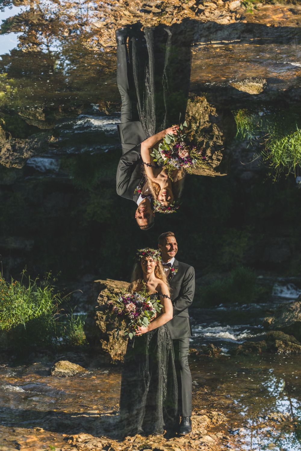 Creative mirror reflection portrait of two people in black dresses holding flower bouquets outdoors.