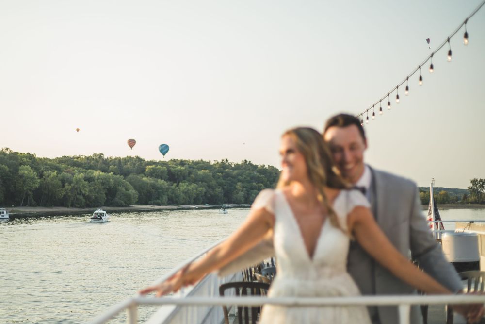 A couple enjoys a romantic moment on a boat deck with string lights and water views.