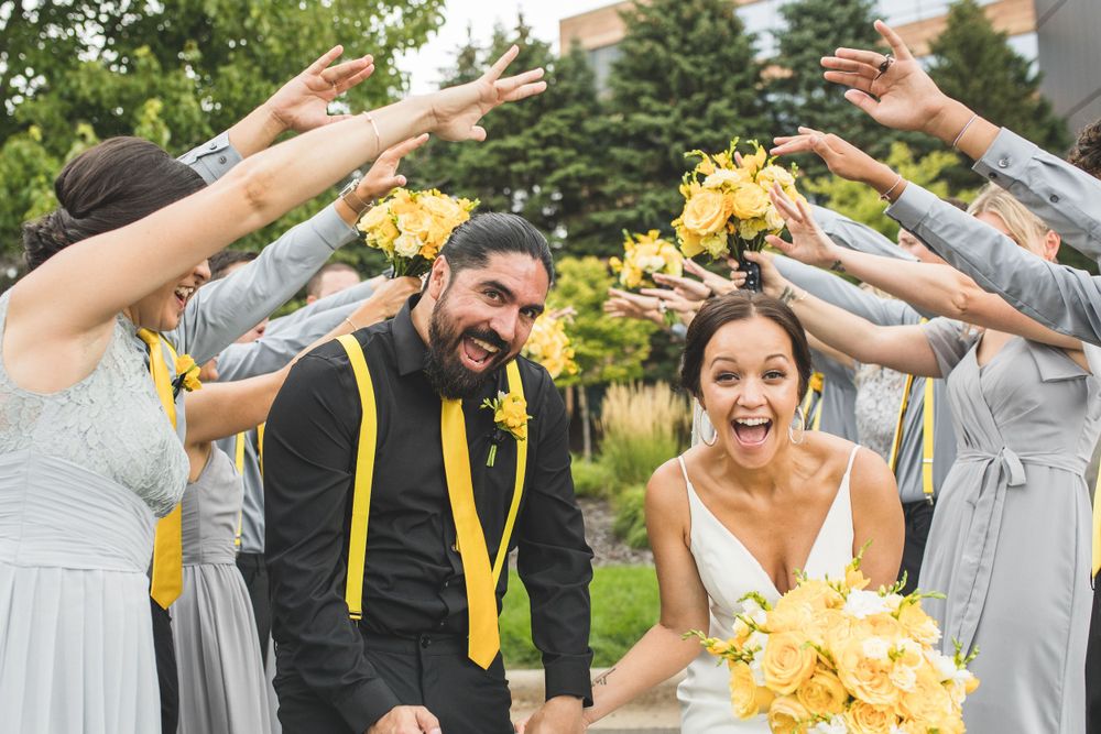 Wedding party creates a tunnel with raised arms while newlyweds walk through holding yellow flowers.