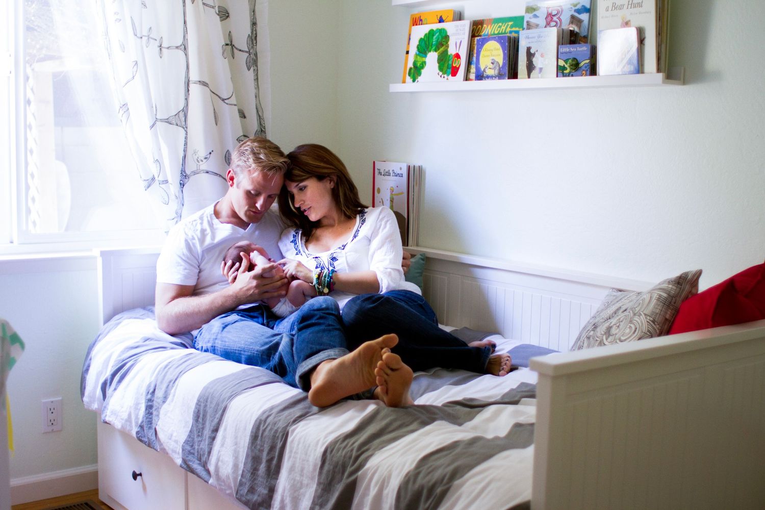 Family sitting on bed in the newborn baby's nursery.