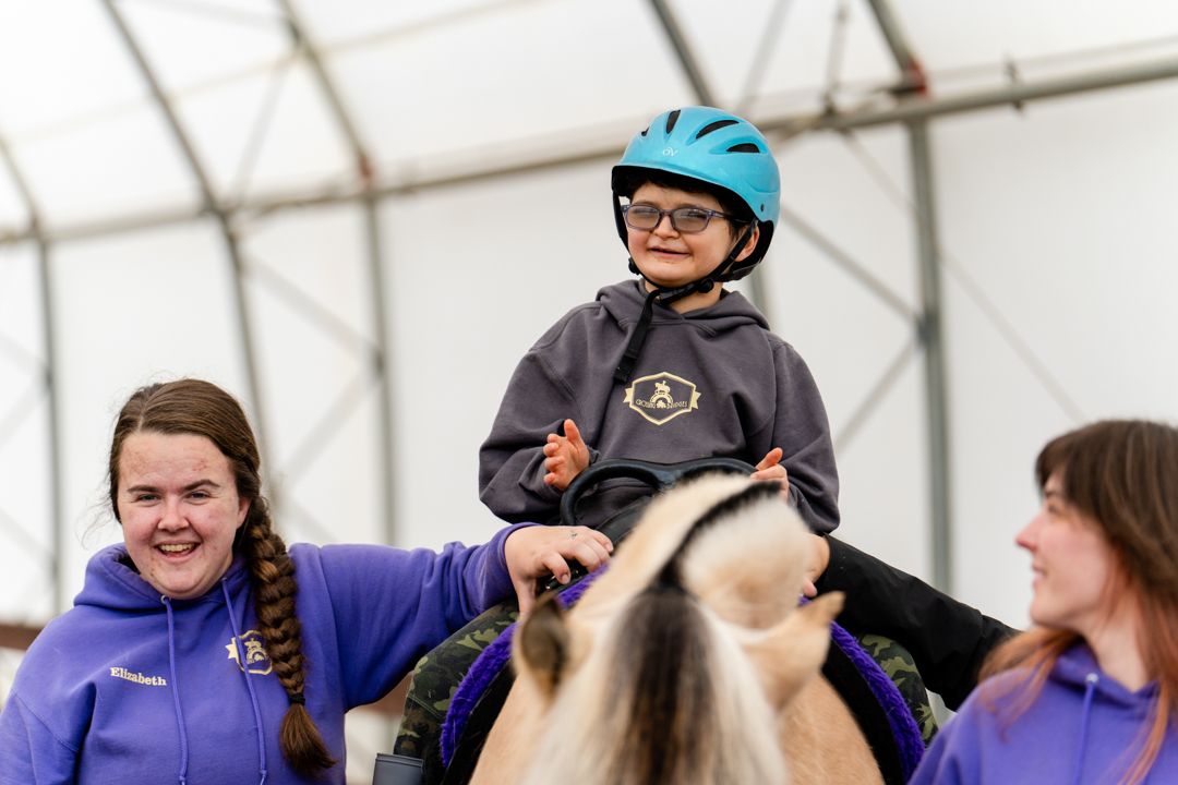 staff laugh with a boy as he rides a horse