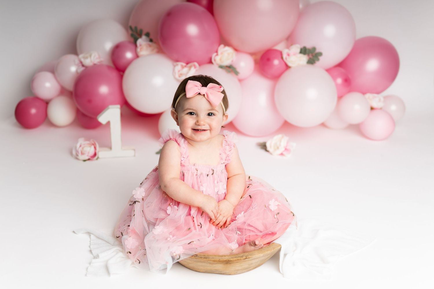 First birthday celebration setup with pink balloon arch and small cake.