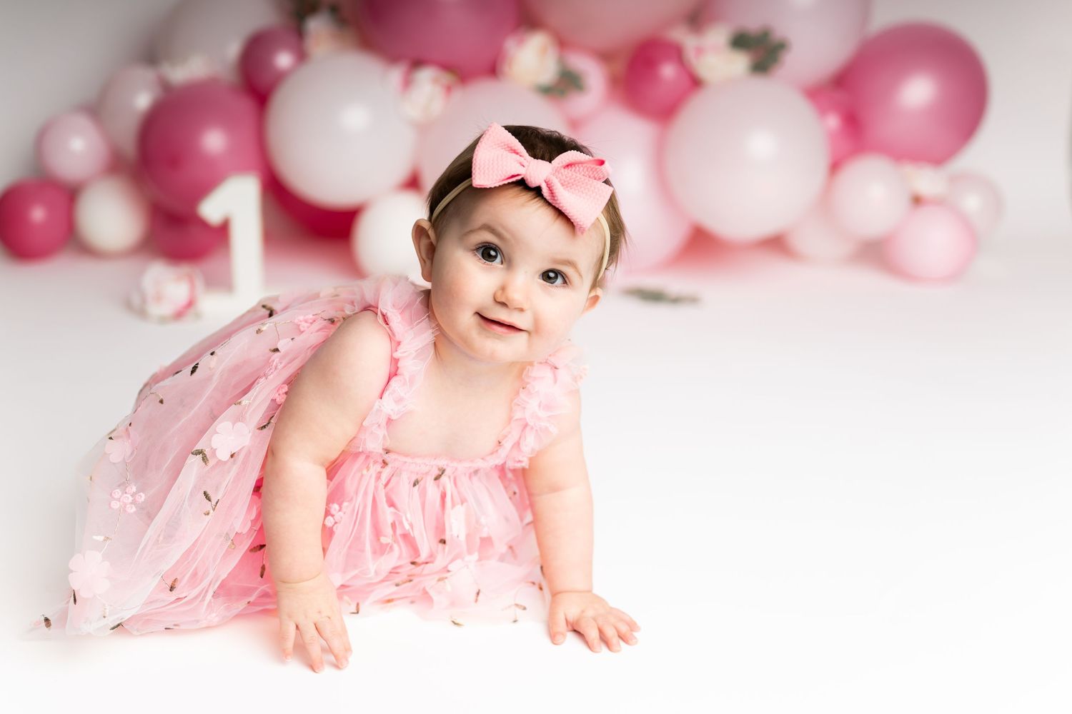 Smiling baby in pink dress posed with pink and white balloon decorations.
