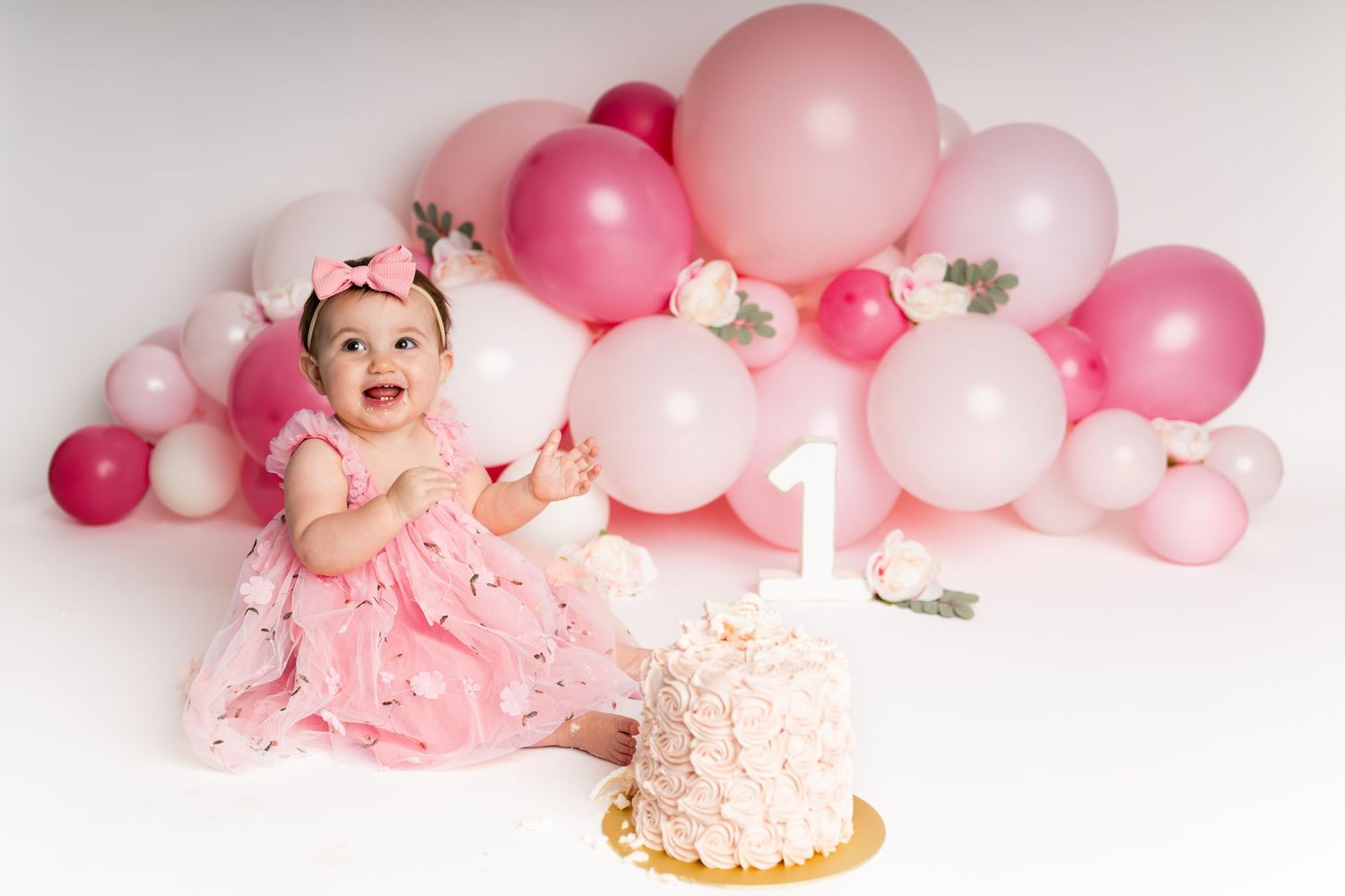Happy baby laughing during cake smash photoshoot with pink balloon decorations.
