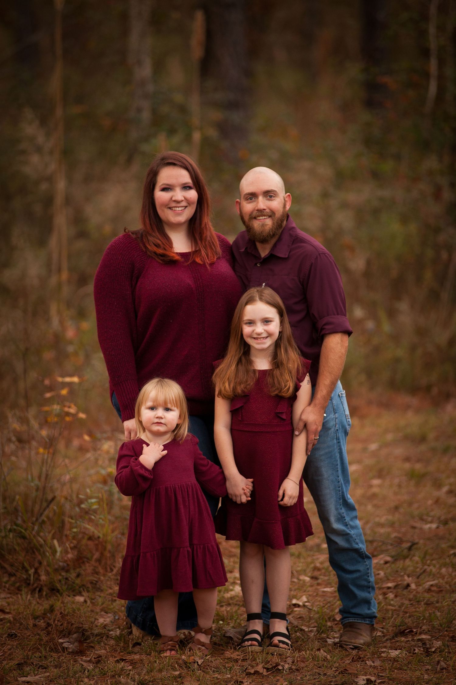 Portrait in burgundy coordinated outfits against woodsy backdrop.