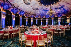 Elegant banquet hall decorated with red and gold accents under ornate domed ceiling.