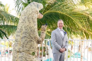 A person in a grey suit poses near a stone pillar with tropical palm trees in the background.