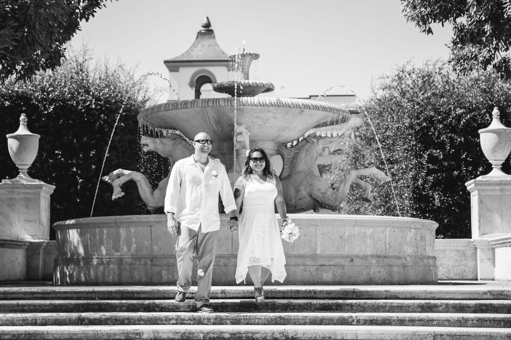 A couple descends elegant stone steps in formal attire at a historic venue.