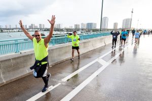 Runners participate in a marathon on a wet bridge with city skyline in the background.