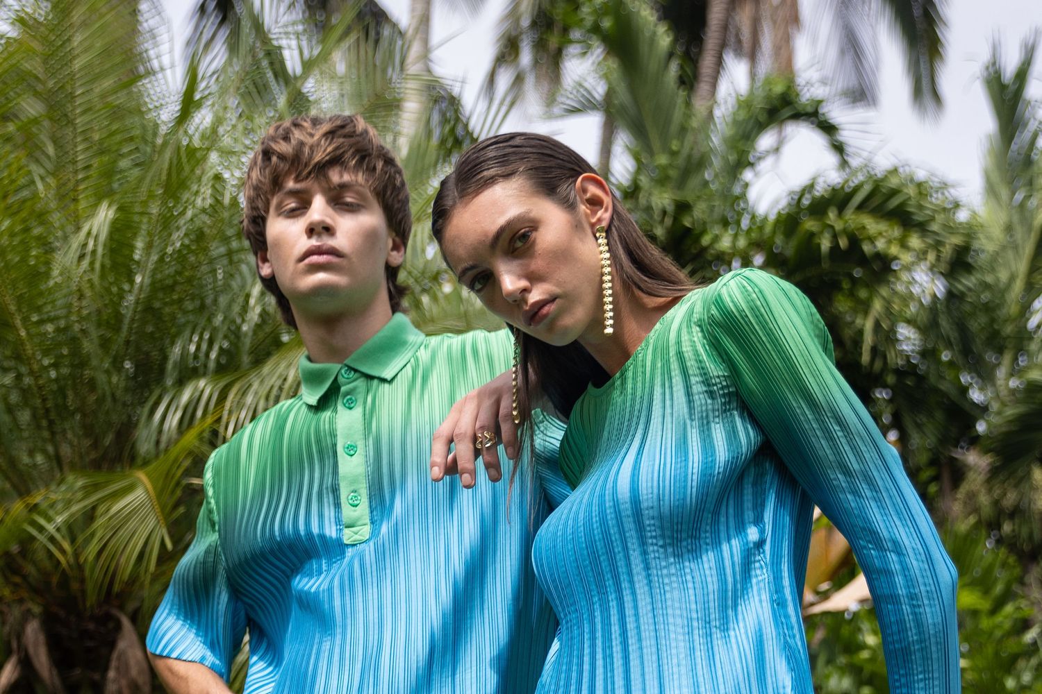 Fashion models in color-gradient activewear against tropical palm background.