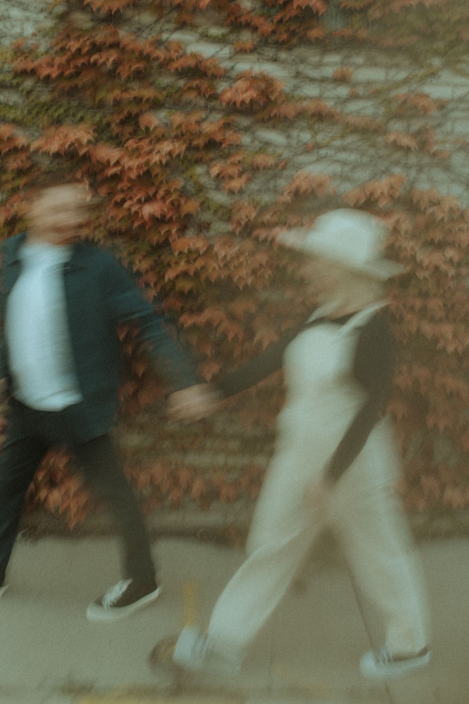 Motion-blurred photo of two people walking past ivy covered wall.