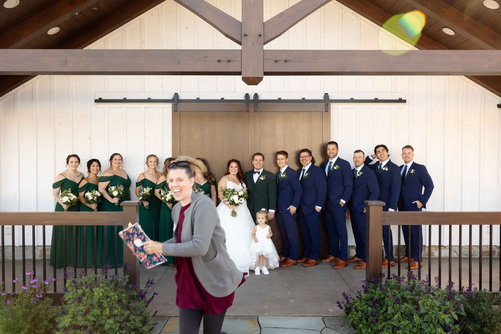 Wedding party posing in front of a rustic venue with bridesmaids in green and groomsmen in navy.