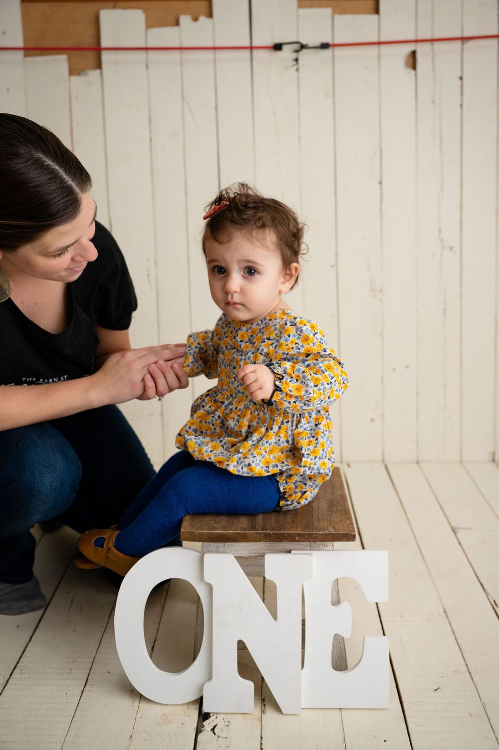 A yellow floral top and large white 'ONE' letters set against white wooden planks for a first birthday photoshoot.