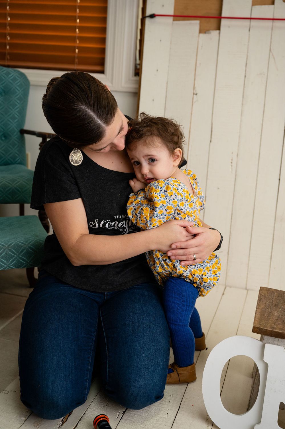 Tender moment between parent and child sitting together with white 'ONE' letters on wooden floor.