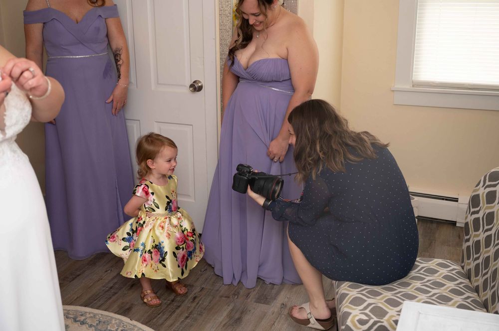Photographer capturing a young child in a floral dress while others look on in purple gowns.