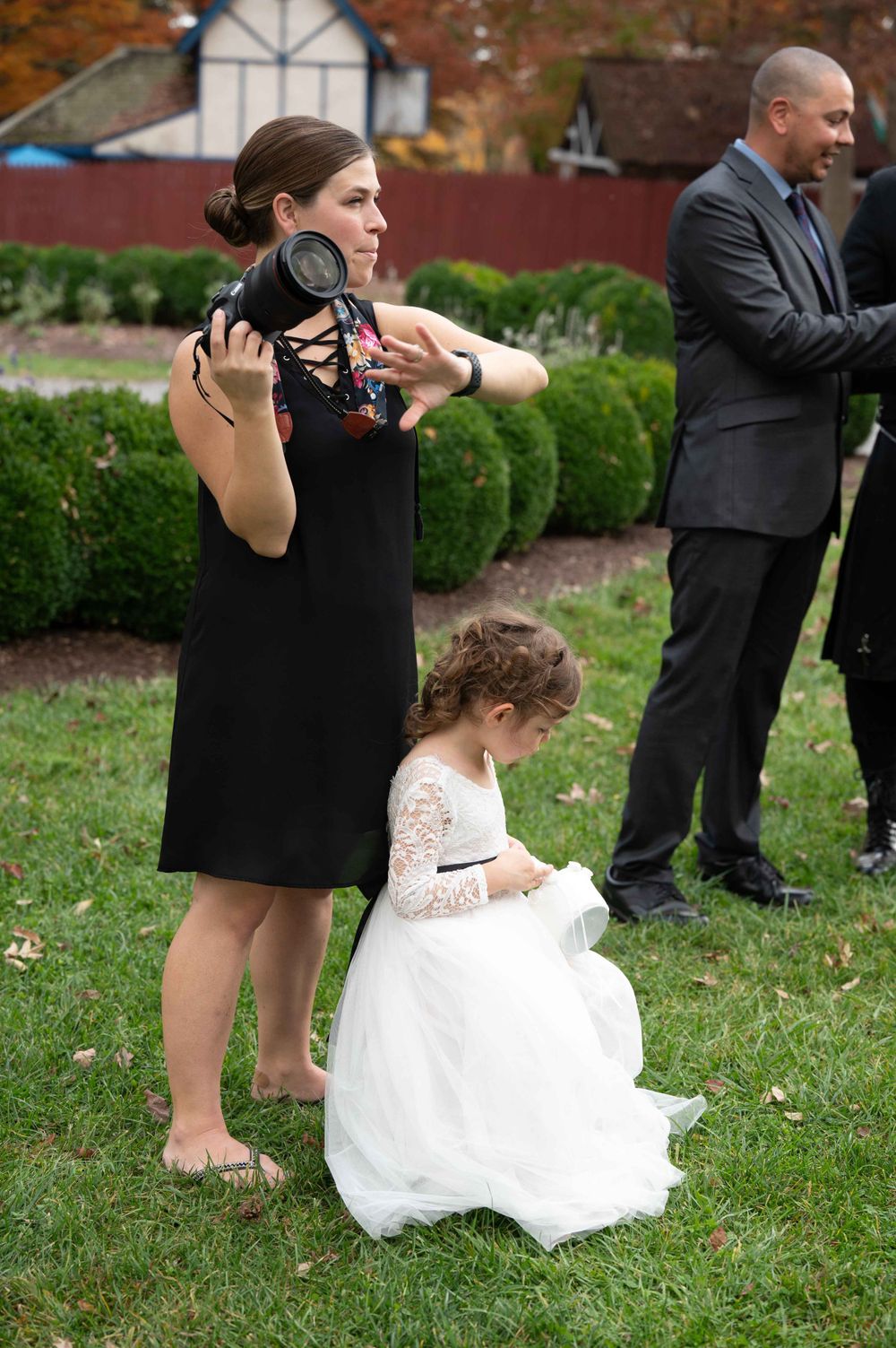 Photographer with camera taking pictures outdoors at a formal event near manicured bushes.