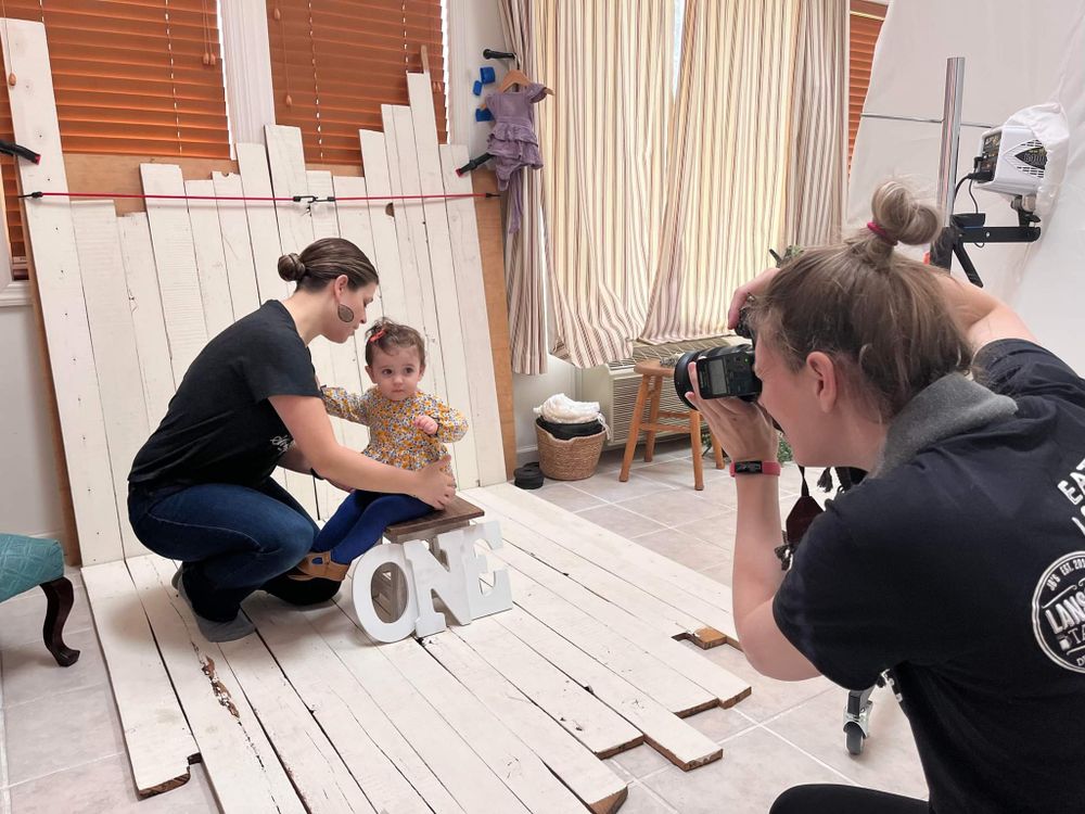 Behind the scenes of a photo shoot with photographer and subjects on white wooden deck.