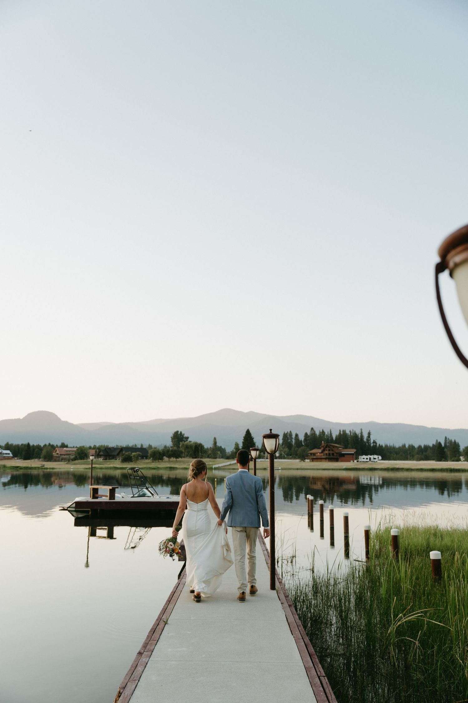 Couple walking on lakeside dock at sunset with mountain vista.