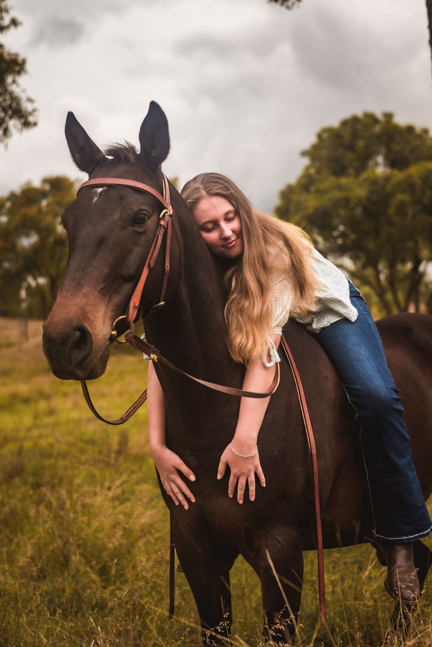 Person bonding with dark horse in rustic field setting.