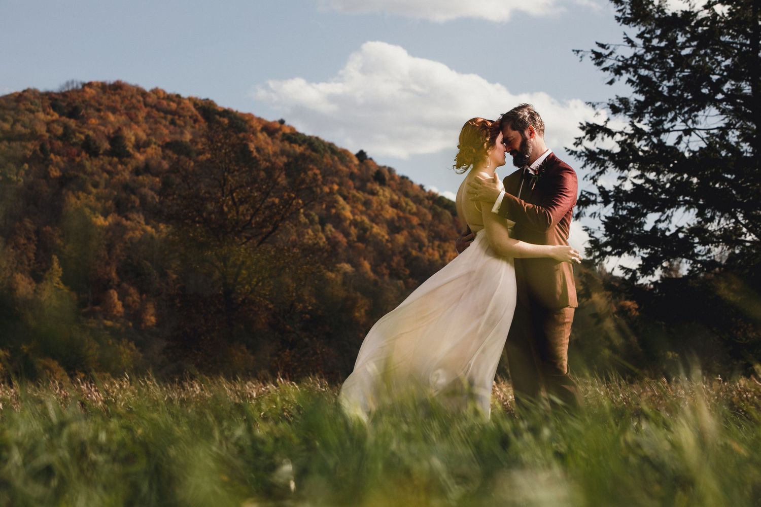 Couple embraces in romantic pose amidst autumn mountain landscape at sunset.