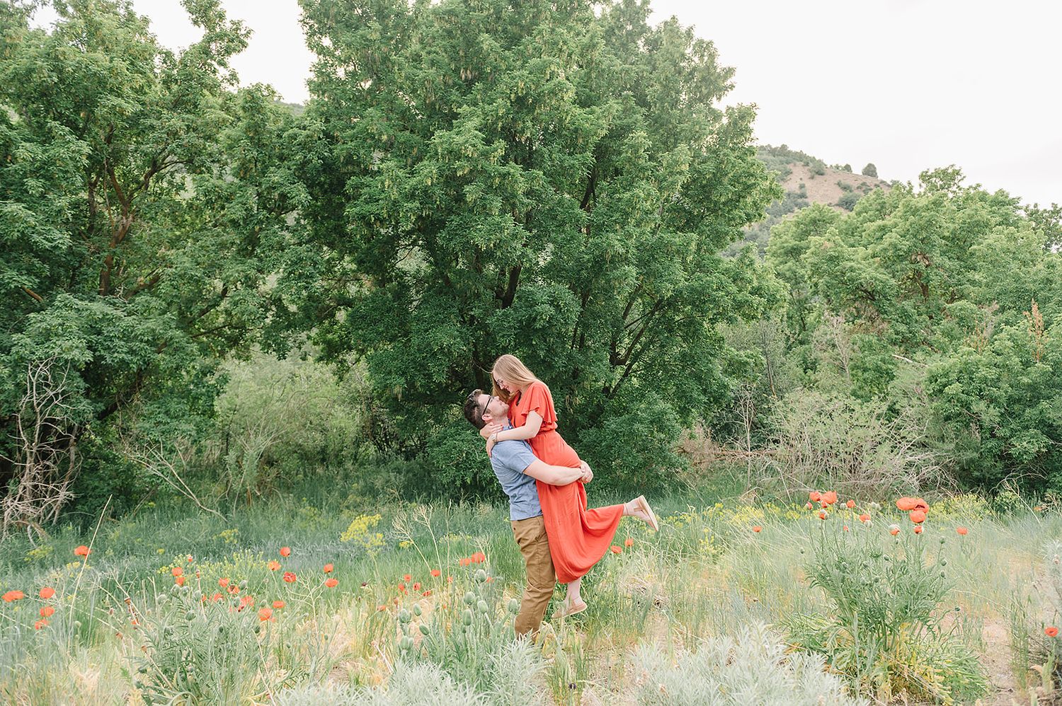 A joyful embrace in a wildflower field with mountains in the background.