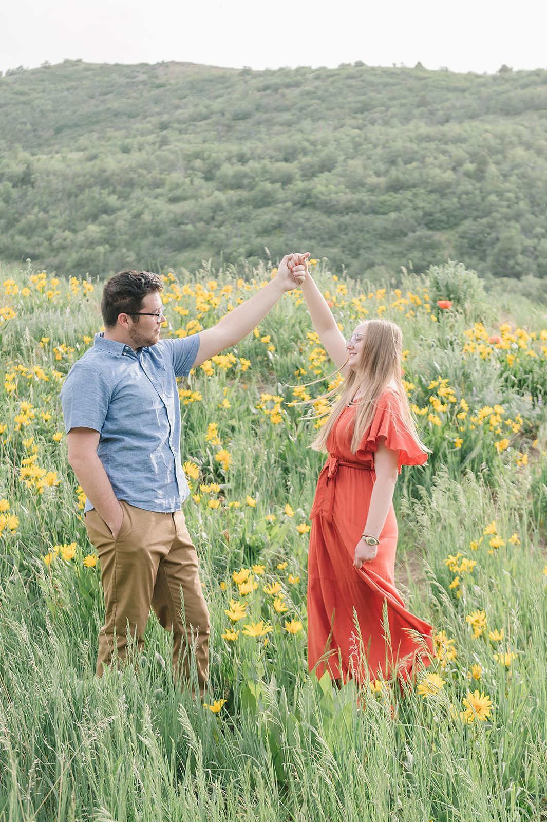 Couple dancing together in a field of yellow wildflowers against rolling hills.