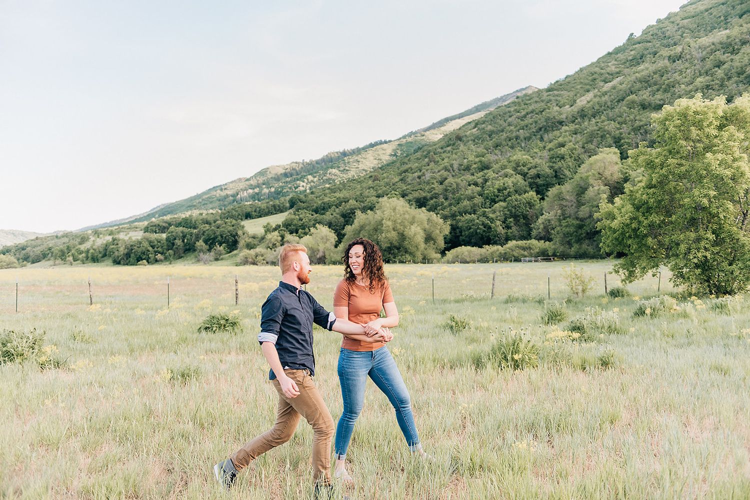 Two people playfully run through a sunny mountain meadow together.
