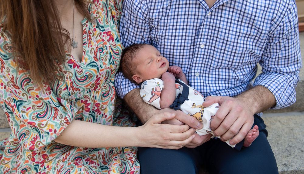 New parents in casual attire tenderly holding their sleeping newborn baby.
