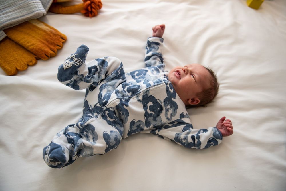 Newborn baby lying on white bedding wearing blue and white patterned sleeper.