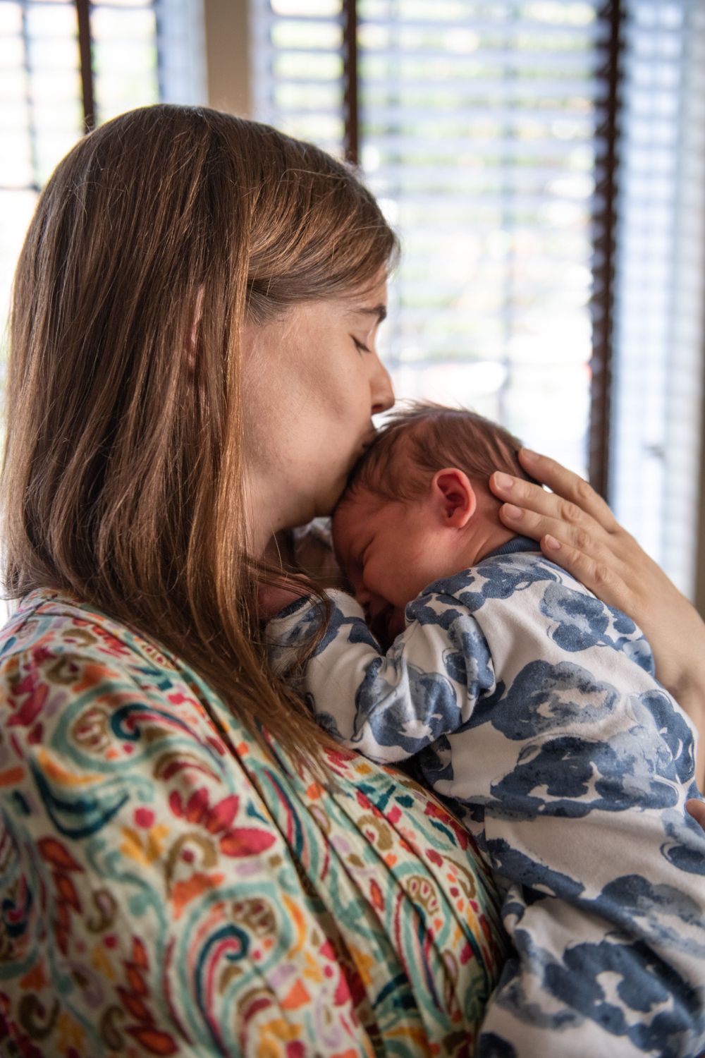 Tender moment captured as baby in blue pattern sleeper receives gentle kiss.