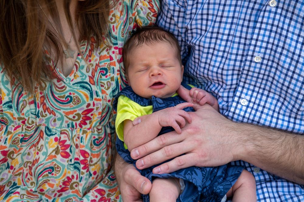 Newborn baby rests between parents wearing floral and plaid patterns.