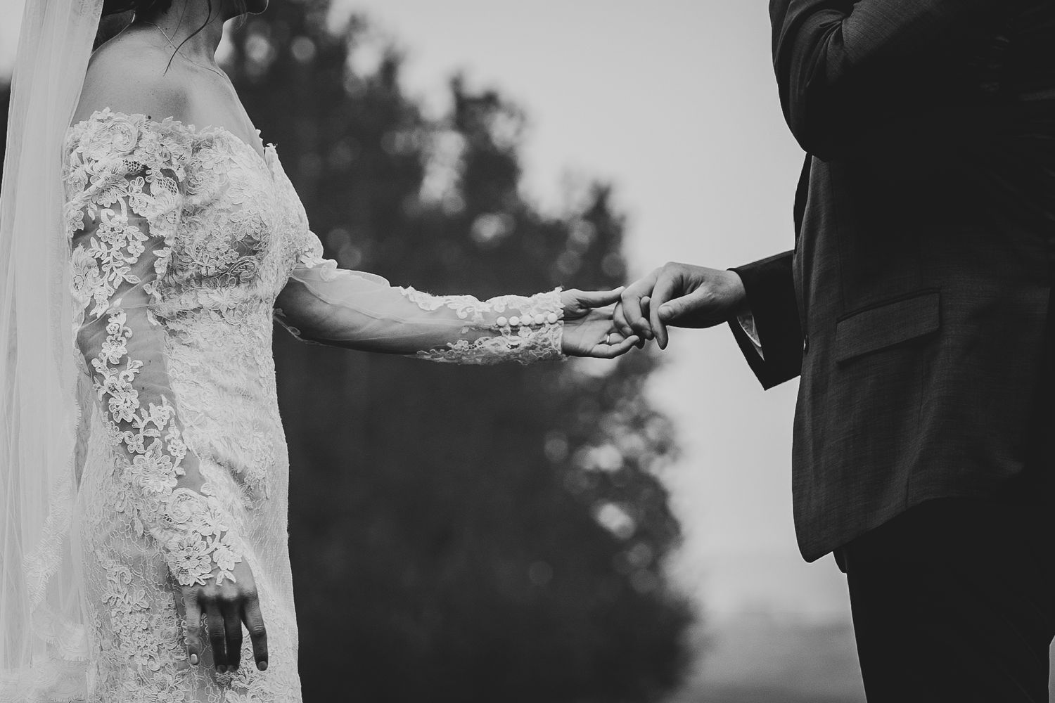 Black and white photo capturing ring exchange during wedding ceremony with detailed lace sleeve.