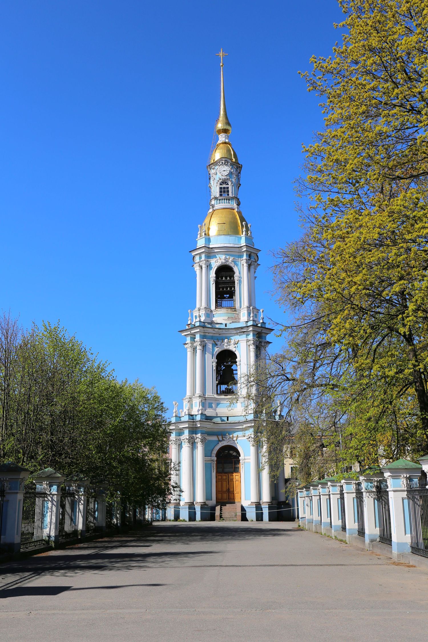 Tall white Orthodox church bell tower with golden dome against bright blue sky.