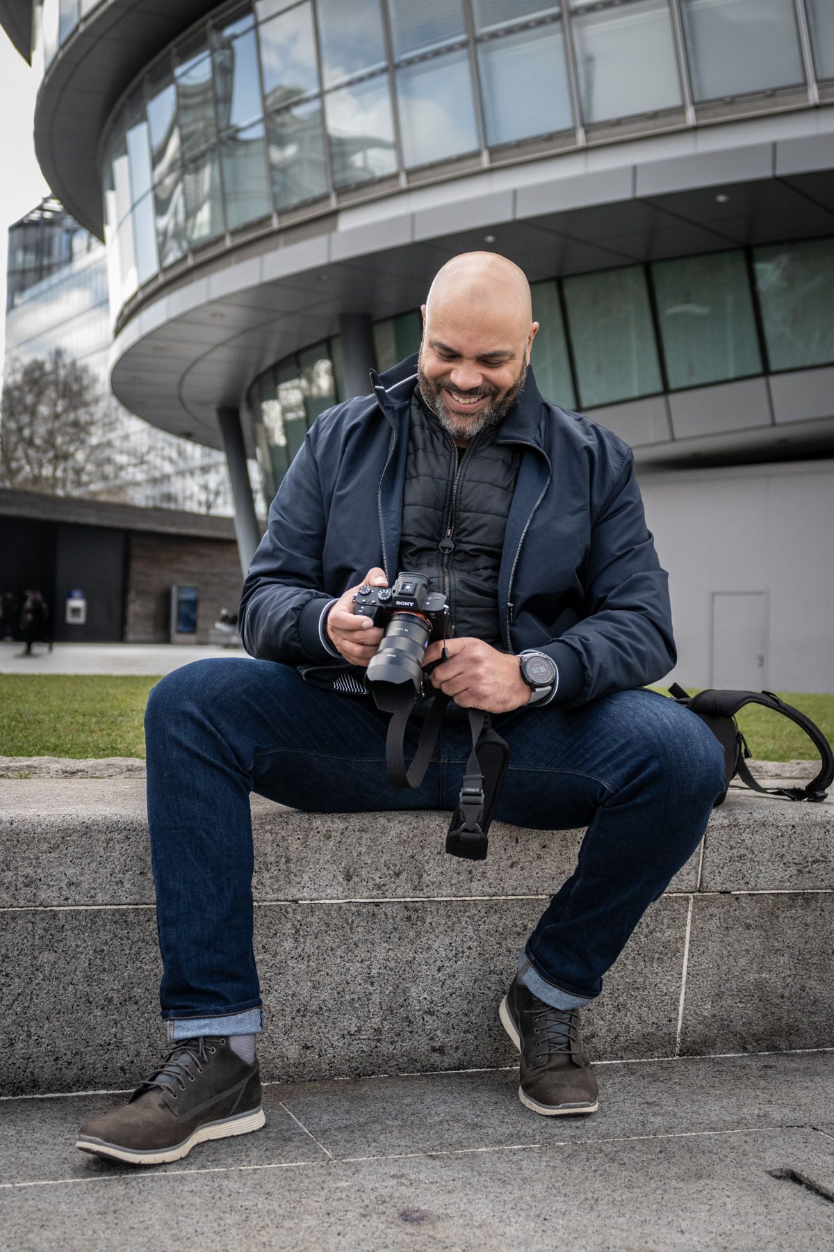Professional photographer reviewing images on their camera while sitting on concrete steps outside a modern building.