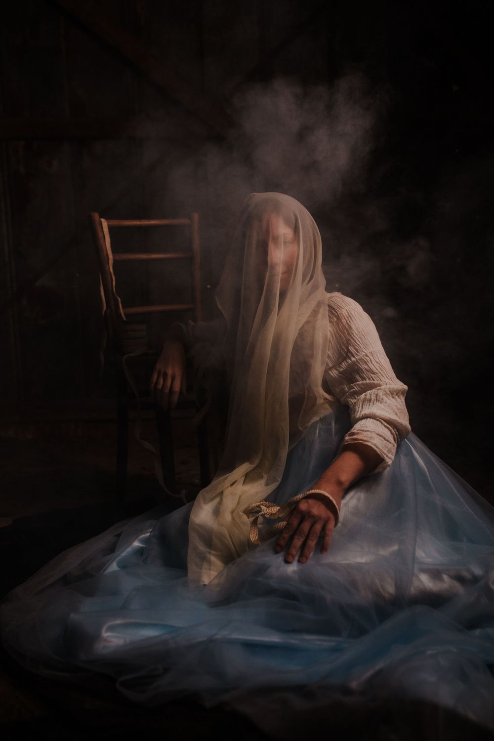 A woman is seated next to a chair with a veil covering her face