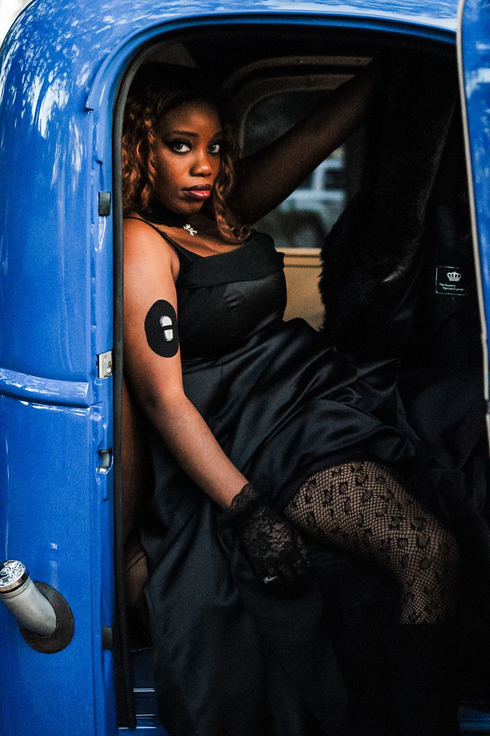 A woman in a black dress looks out of the inside of a blue pickup truck